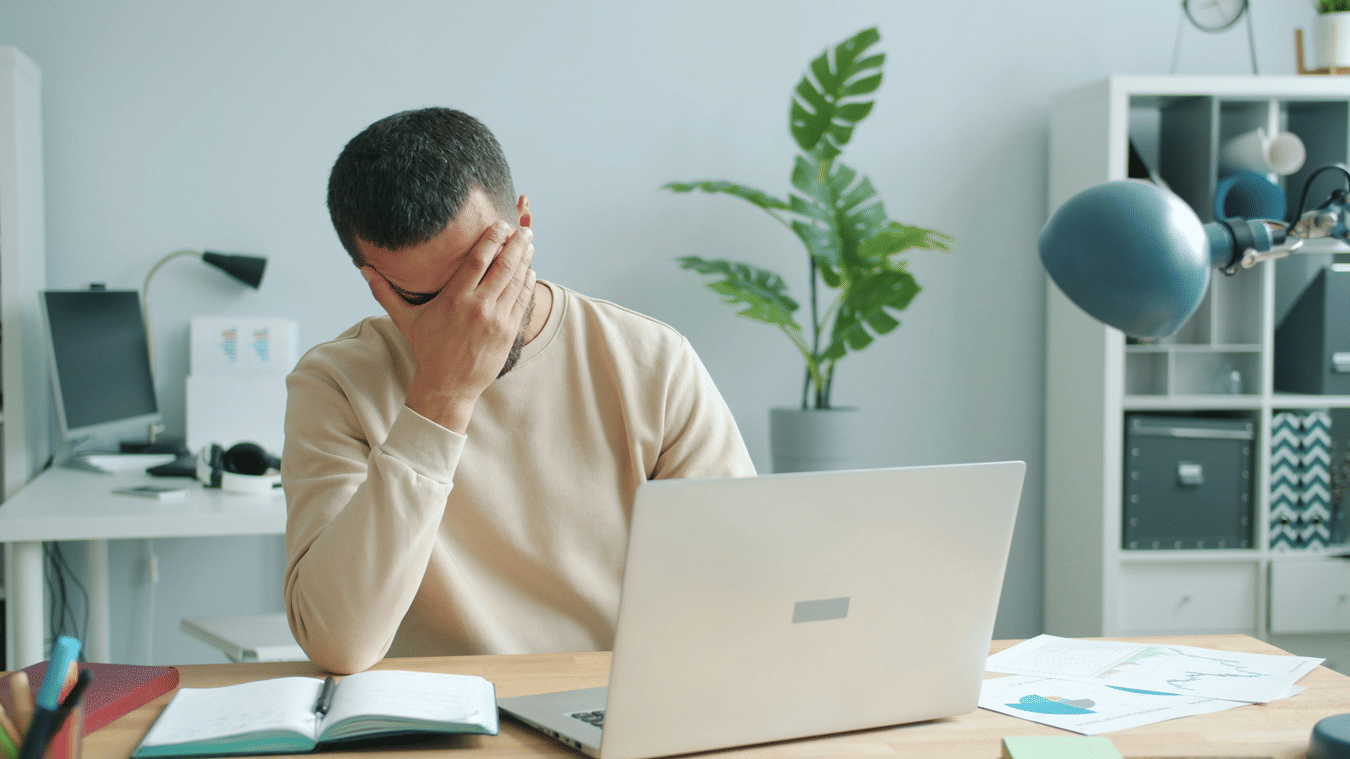 a stressed out person holding their head sitting in front of a laptop