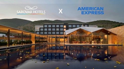 A building with several windows, restaurant with glass walls, and a corridor with plants and lights. A promotion for Amex Card holders at Sarovar Hotels.