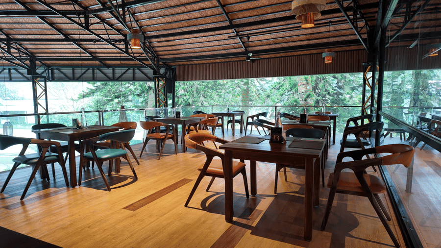 Open-air Above Clouds Bar at DNC Shevaroys Resort & Spa with wooden tables and chairs set on a polished floor under a timber-framed roof.