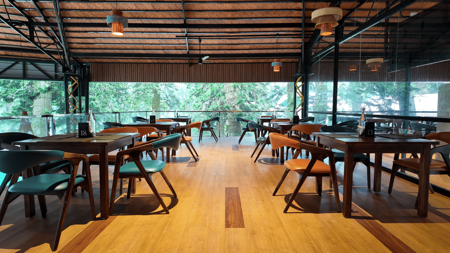 Open-air dining area at DNC Shevaroys Resort & Spa with dark wood tables and teal chairs overlooking greenery.