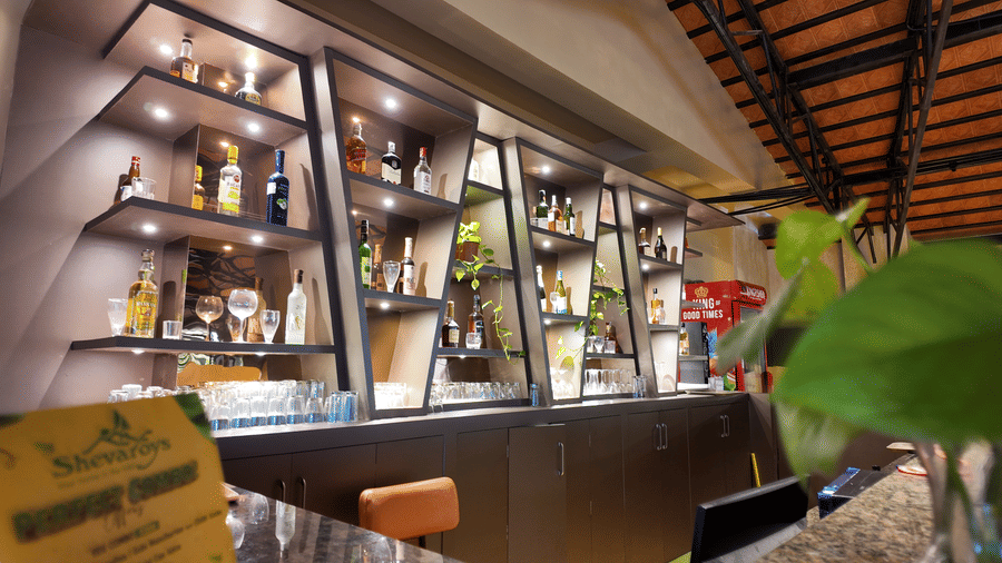 Close-up of the bar area at DNC Shevaroys Resort & Spa with illuminated glass shelves displaying various bottles.