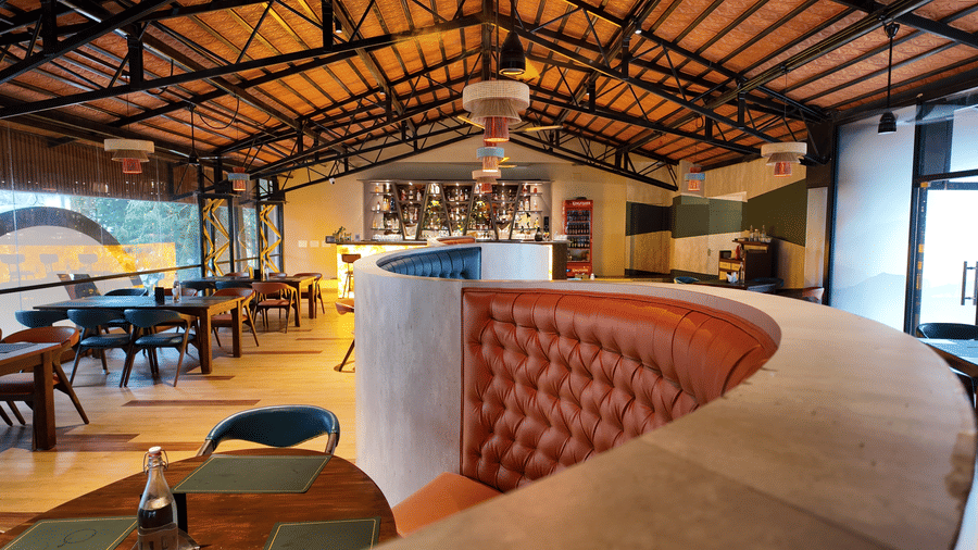 A curved tan leather booth seat in the dining hall of DNC Shevaroys Resort & Spa with a view of the bar.
