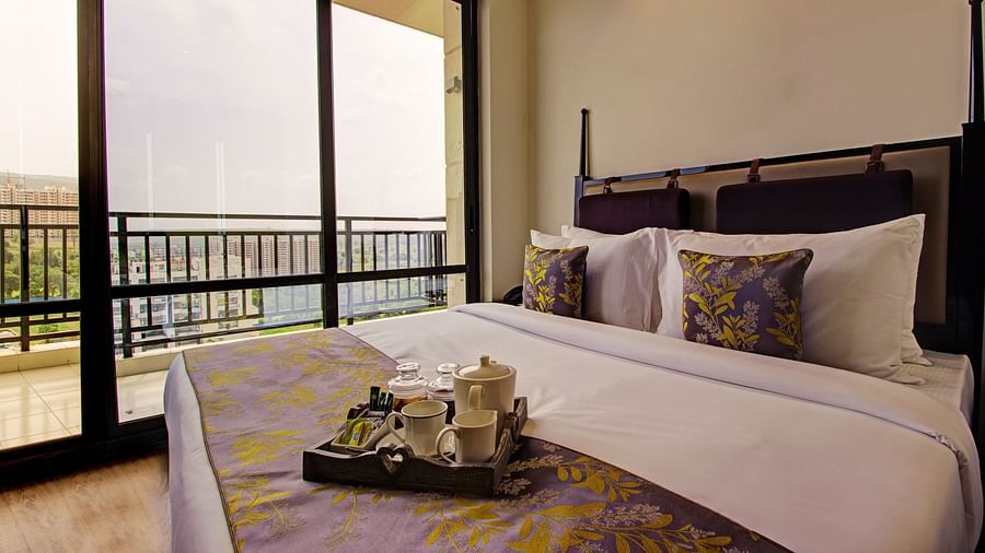 A plush king-size bed placed next to the door to balcony and a tray with cutlery for hot beverages placed on the bed runner