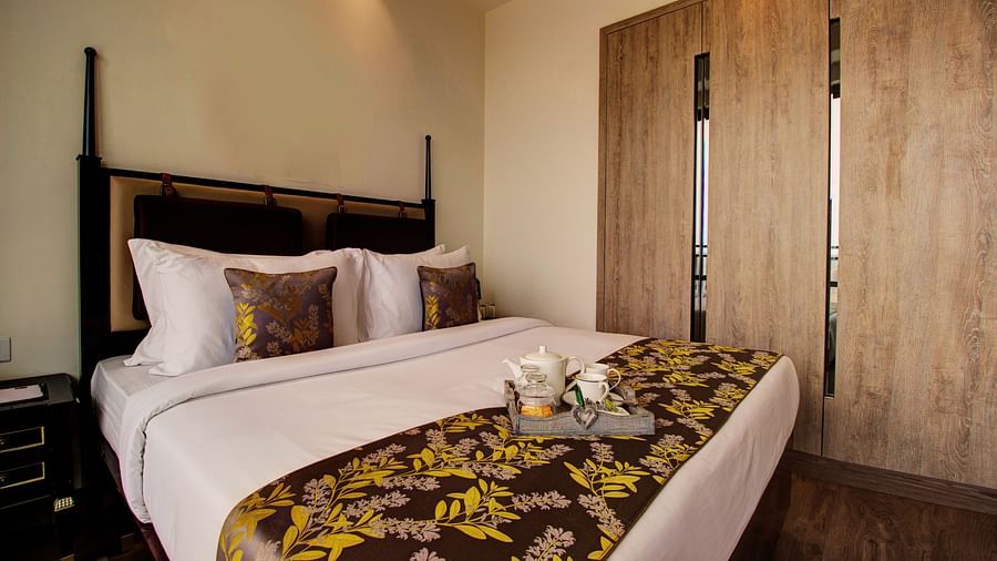 A plush bed on with pillows and cushions and a tray containing cutlery for hot beverages sitting on the bed runner with a large closet in the background