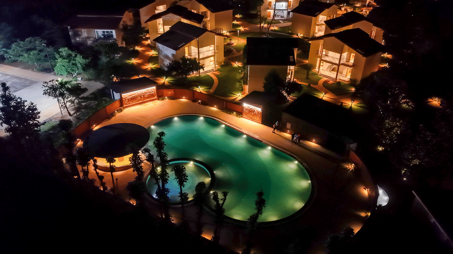 A night-time high-angle view of an illuminated swimming pool surrounded by resort cottages lit up at night | Lords Sahyadri Resort, Shivamogga