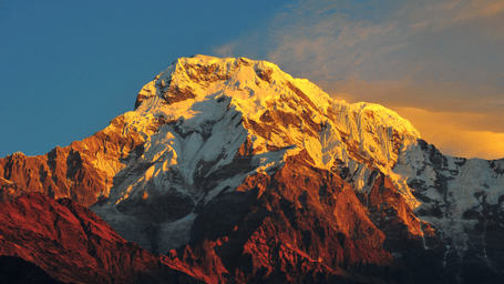 A view of a snow covered mountain peak illuminated by the warm golden light of a sunset.