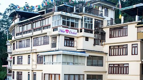 The exterior of New Orchid Lords Inn Gangtok  is shown during the daytime, nestled on a hillside with multiple stories and windows.