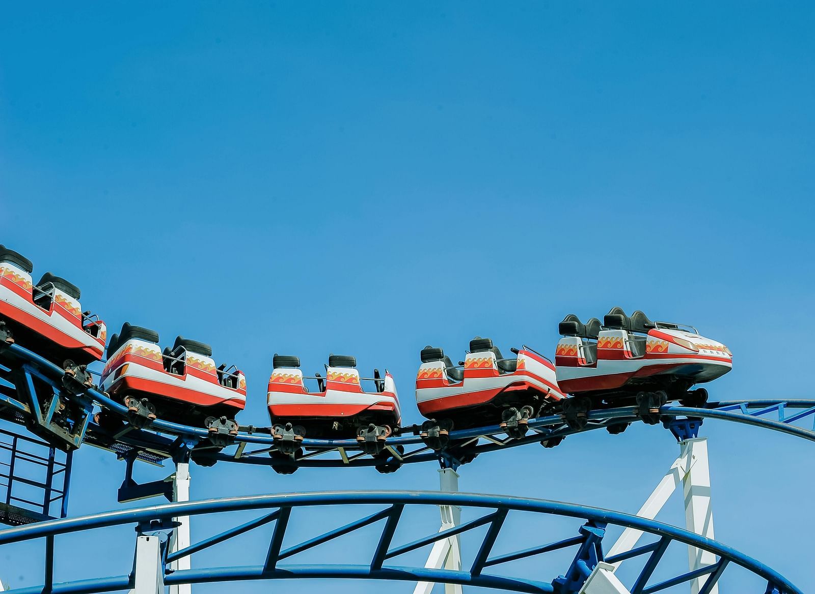 A red roller coaster train on a curved track against a bright blue sky.