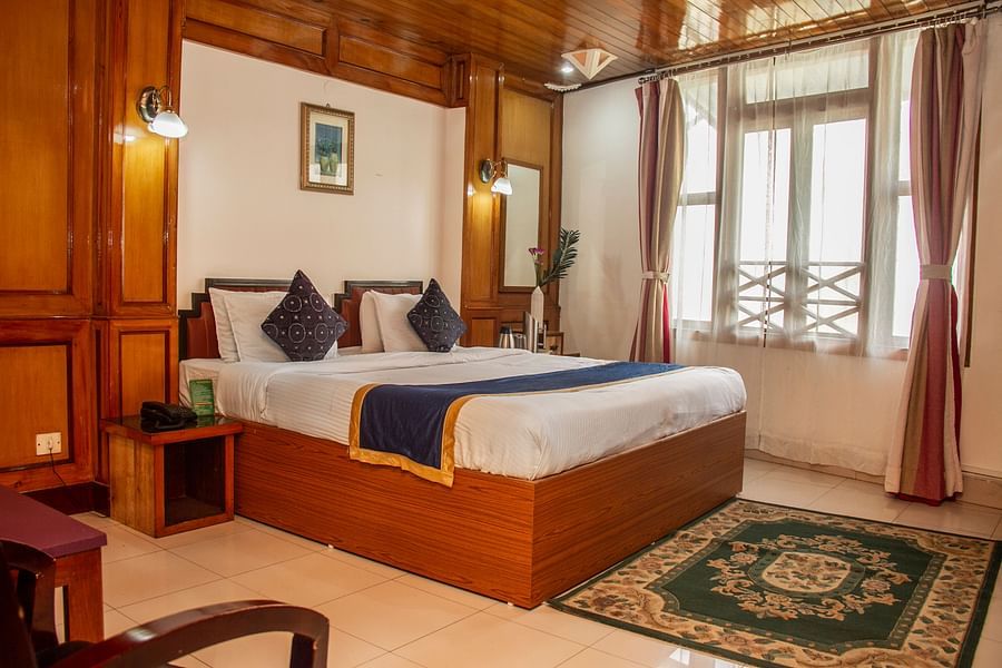 An image of a Hill Club room featuring a double size bed, a bedside table, jug, tea and coffee maker on the other table, and a mirror at Central Hill Resort, Gangtok