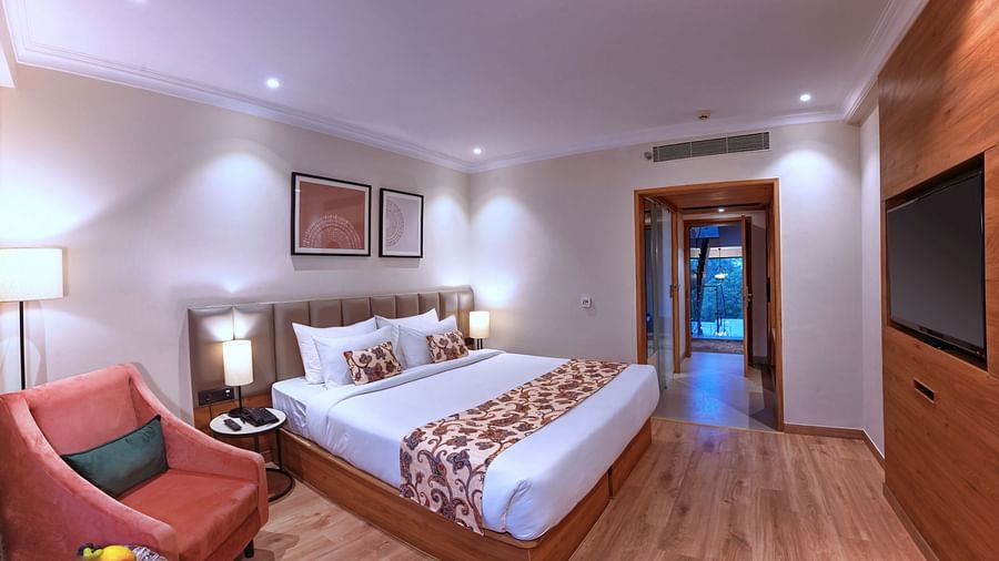 A room featuring a bed, wall paintings, lamps, sofa chairs and a TV - Royale Sarovar Portico, Agra