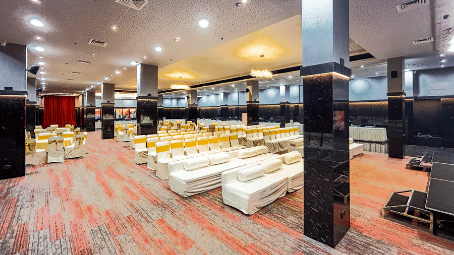 Spacious banquet hall with carpet flooring, sofas, and stage seating at Infiniti Hotel, Indore.