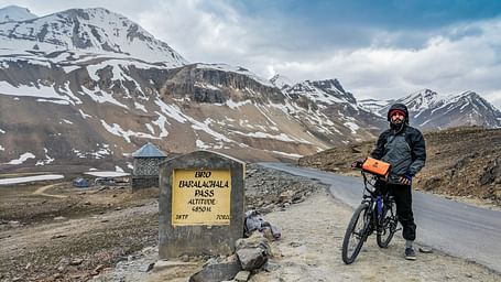 A biker posing with their bicycle at a high-altitude road sign