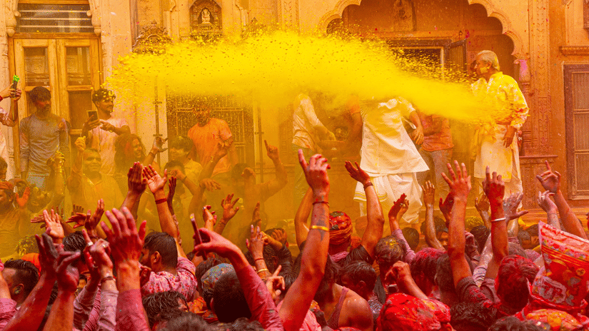 People celebrating the festival of Holi with yellow powder colour thrown in the air over them.