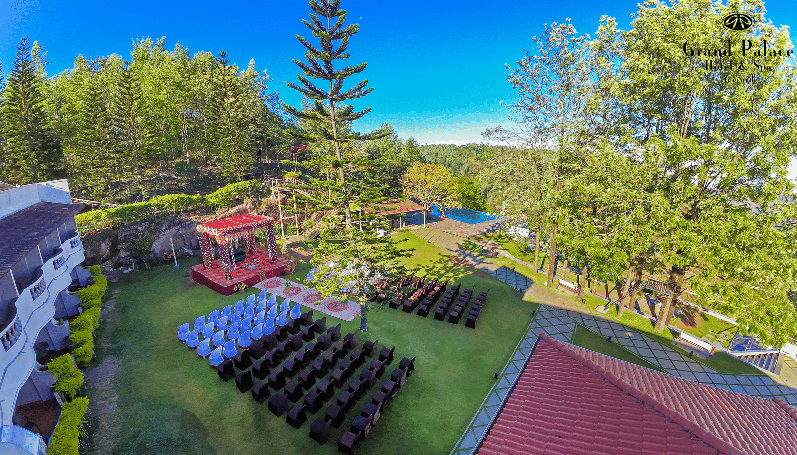Lawn and trees with outdoor seating arrangement, flowerbeds, and children’s rides at Grand Palace, Yercaud, as seen from above.