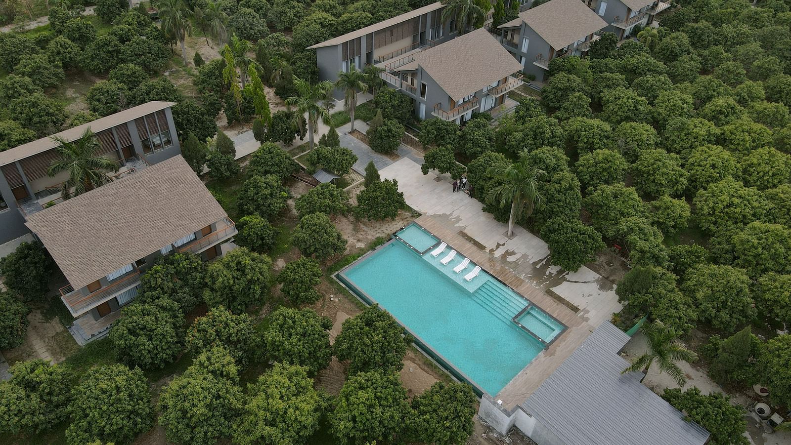 Aerial view of a rectangular swimming pool amidst dense greenery with villas arranged symmetrically around it at Wyndham Garden.