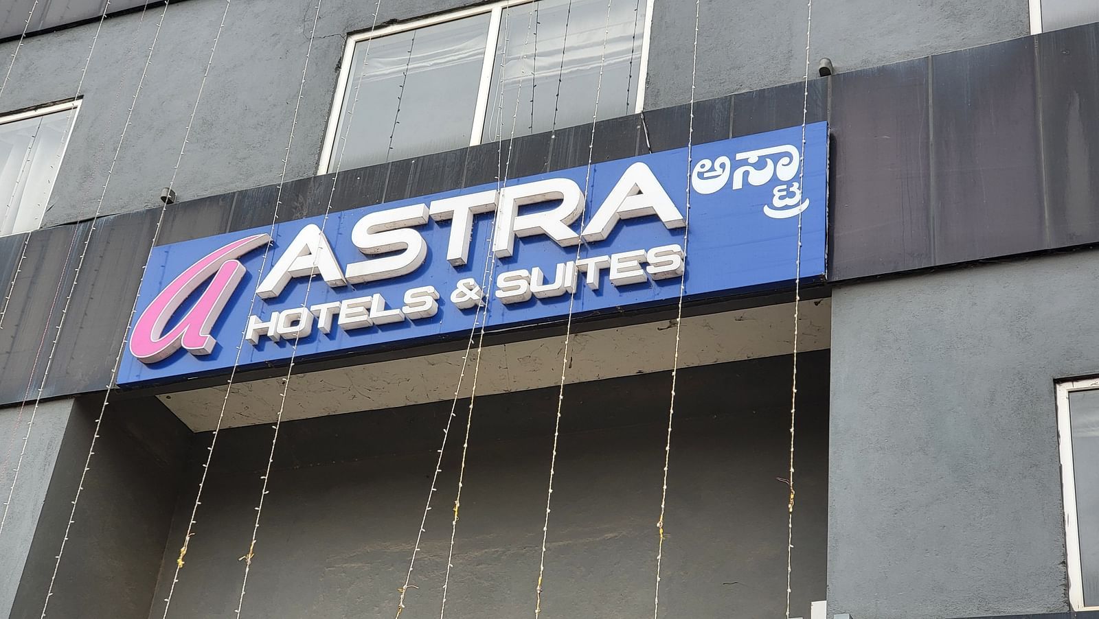 The exterior signage of Astra Hotels & Suites, a modern black building with a bold blue and red sign - Astra Hotels & Suites, Sarjapura