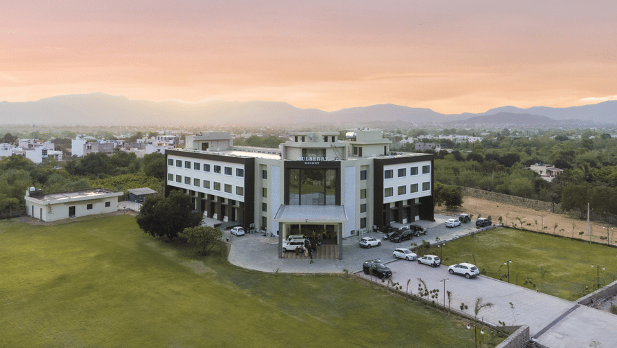 A facade of Bamboo Saa Mulberry Resort, Pushkar, with the building, garden area around it, and evening sky in the backdrop.