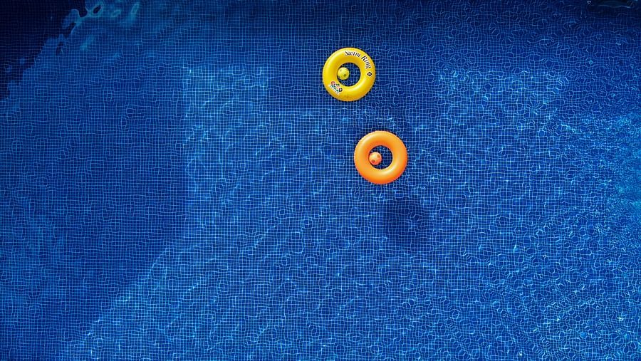 Two floats on inflatable rings in a blue swimming pool, seen from above | Woodstock Resorts, Coorg