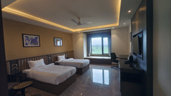 A spacious hotel room at Pride Resort, Jodhpur, with two beds, a TV, and large windows providing natural light.