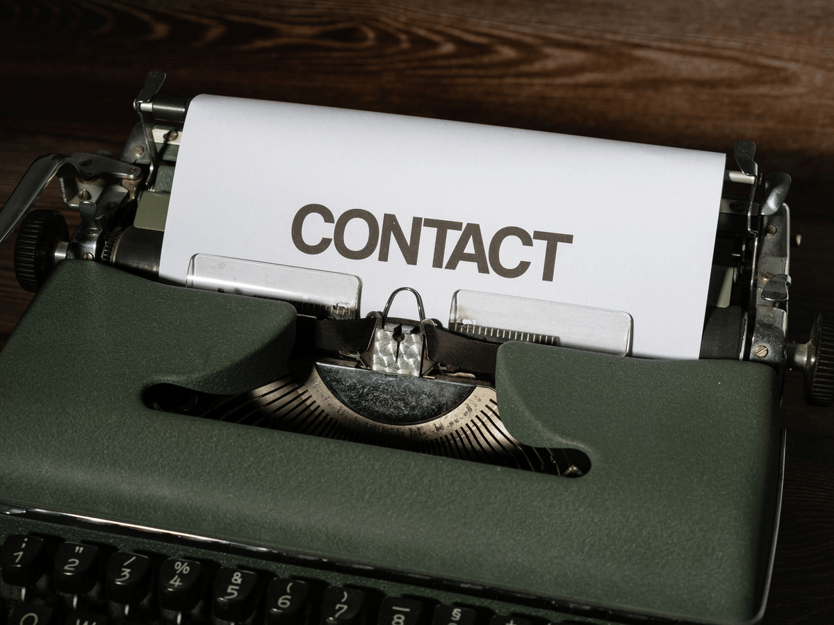 A vintage typewriter with a sheet of paper reading contact