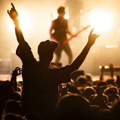 An image of a concert with a musician playing the guitar on the stage and the crowd cheering for him.