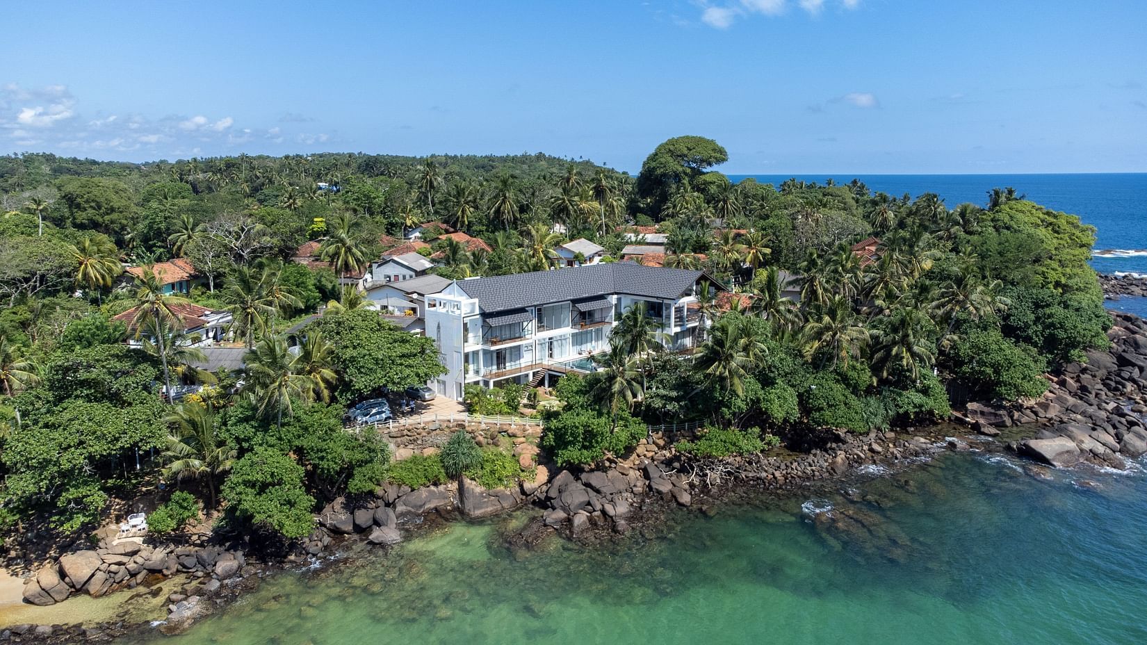 facade image of the Beacon by the Bay Villas and Suites nestled amidst a lush green tropical forest with a vast blue sea in front of it