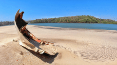remnants of a boat on Querim beach with brown sands and land in the background