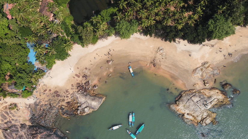 An aerial shot of a beach with blue boats near the shore