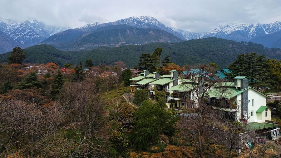 Aerial view of a green estate with houses amidst richly colored forests and mountains in the background.