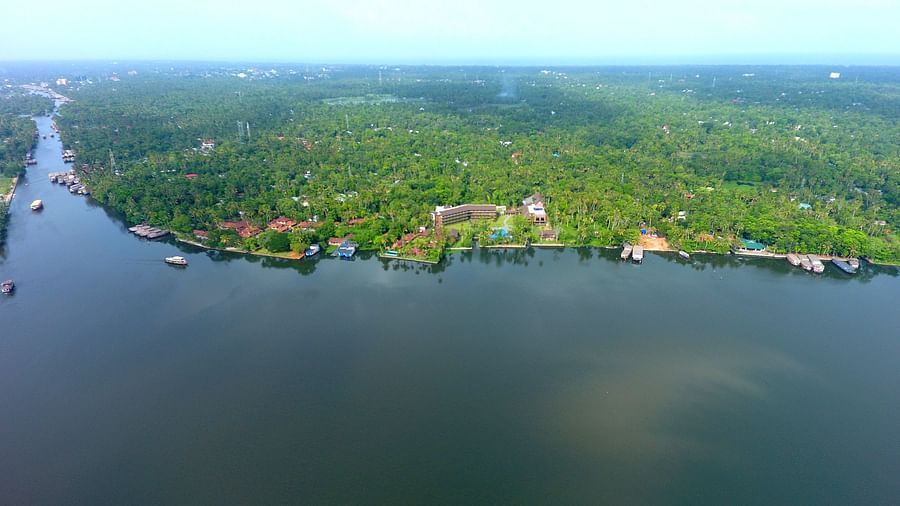 lakeside landscape of Alappuzha with lush greenery, scattered resorts, and boats navigating the calm waters under a clear sky