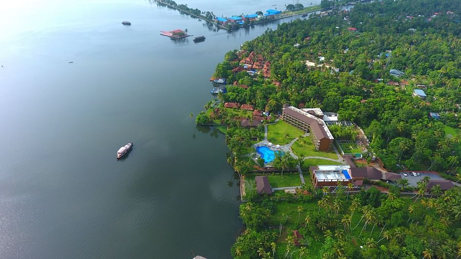 Uday Backwater Resort with lush greenery, a swimming pool, and boats on calm waters, offering a tranquil retreat