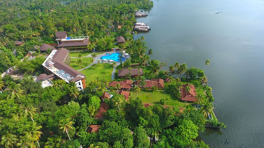 Uday Backwater Resort surrounded by lush greenery, featuring a swimming pool, traditional cottages, and serene waterfront scenery