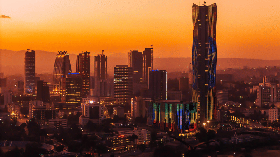 City skyline at sunset, featuring modern skyscrapers and a prominent glass tower.