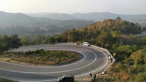A sharp hairpin bend on a hilly road with vehicles and hills in the distance.