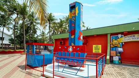 Colourful kids' Graffity tower ride at MGM Dizzee World, set against a vibrant red building with palm trees in the background.