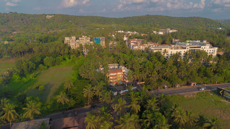 An aerial view showcasing a large hotel complex nestled among green fields and palm trees under a bright sky - Perfectstayz Premium Goa Continental