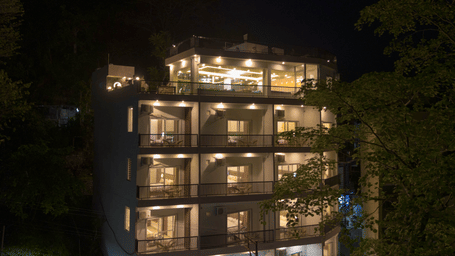 A multi-storey building exterior at night, with windows lit up and trees surrounding the structure in Perfectstayz Premium Mystic Falls, Rishikesh.