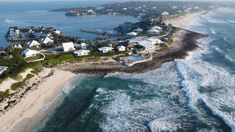 Aerial view of coastal strip near Abaco Inn, with ocean waves, lagoon calm, and seaside homes nestled between rocky shores and sandy beaches.