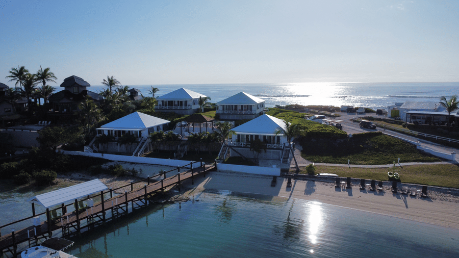  Coastal cottages in Abaco Inn, surrounded by tropical greenery, poolside leisure spaces, and sandy beach with ocean waves reflecting golden light.