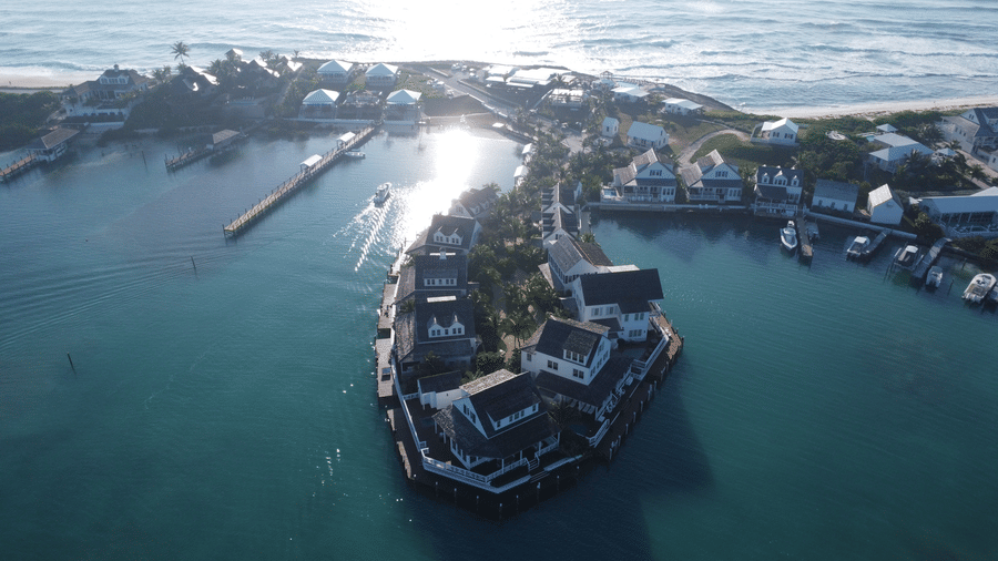 Villas near Abaco Inn seen from above, clustered along turquoise waters with docks, boats, and sunlit reflections creating a picturesque marina setting