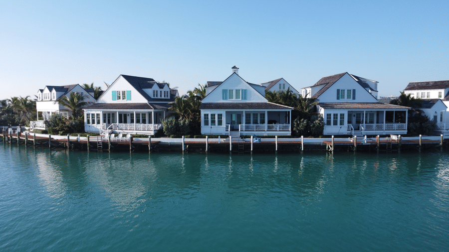 Front view of Sunset Point in Abaco Inn, showcasing waterfront houses with white exteriors, palm trees, and reflections on calm turquoise waters.