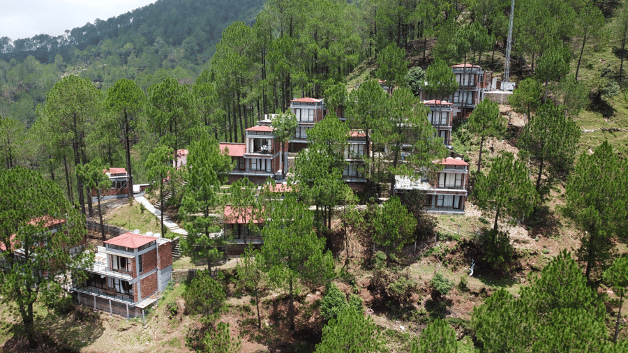 Aerial view of BluSalzz Escapade Resort, Lansdowne featuring buildings adjoining each other and is set on the hills surrounded by trees.