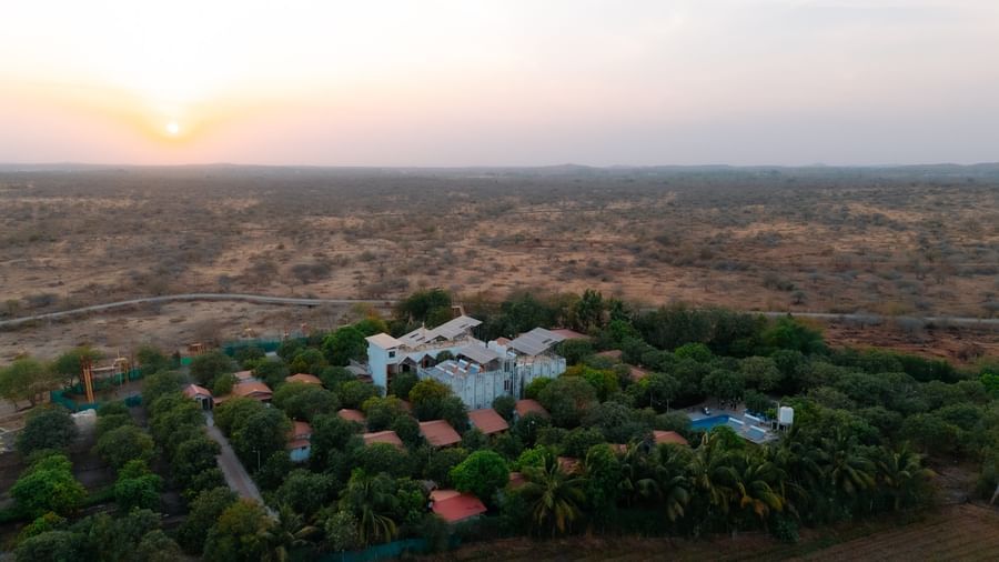 An aerial view of Daksh Resort & Amusement Park, Sasan Gir surrounded by greenery and a view of the sunset at the backdrop.