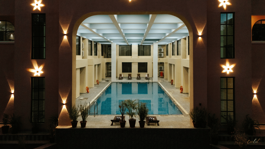 A symmetrical view of an indoor swimming pool at night illuminated by warm wall lights | Daksh the Fateh Retreat