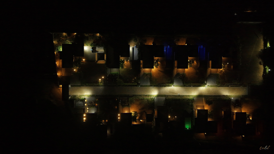 An aerial night view of the resort grounds featuring glowing warm lights along the paths and villas - Daksh The Nirvana Retreat, Pavagadh