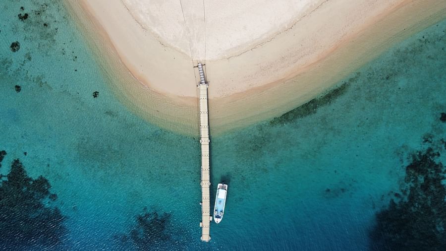 Aerial view of a white sand beach and boat docked at a pier near Flower Island Resort.