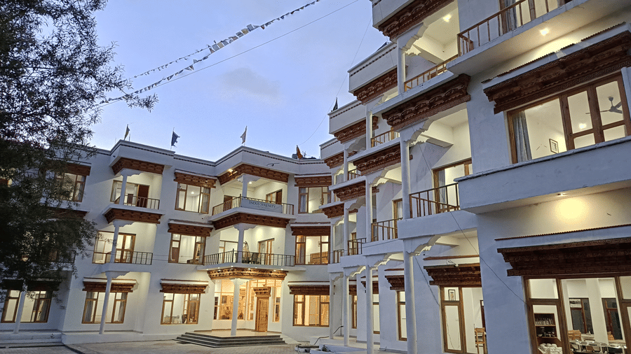 Exterior view of Indus Serenity Retreat, Ladakh featuring a multi-storey white facade with wooden balconies and warm evening lighting.
