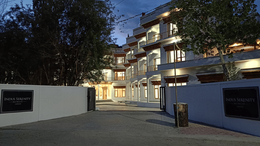 Entrance driveway view of Indus Serenity Retreat, Ladakh captured during dusk with softly lit building exteriors and surrounding trees.