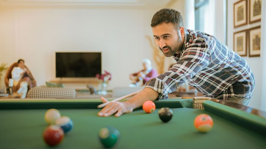 Guest playing a game of pool inside Karma Chalets, with a green pool table and indoor seating area in the background.