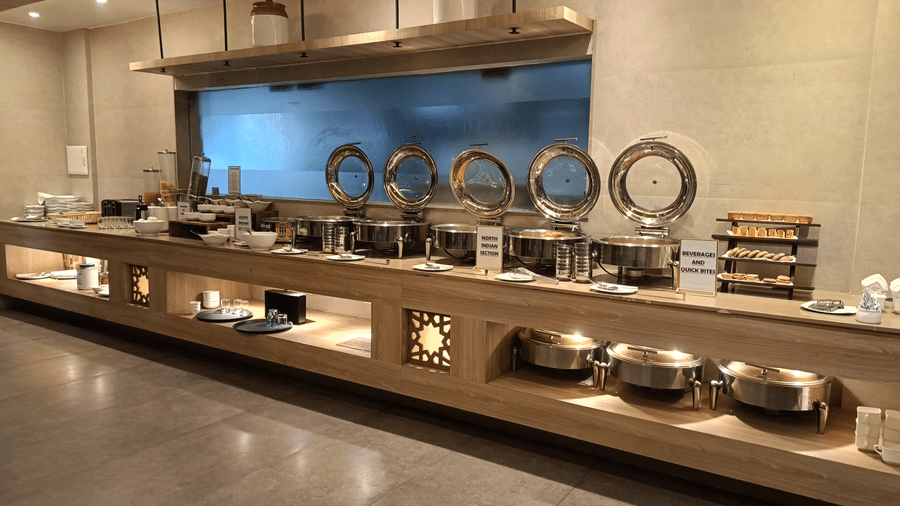 A long buffet station with several silver chafing dishes and serving trays on a wooden counter